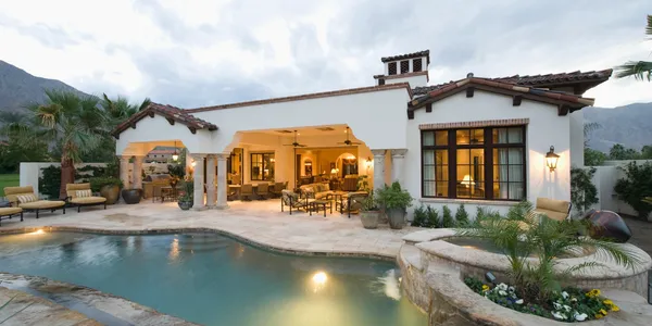 Spanish-style home at dusk with a lit pool and covered patio