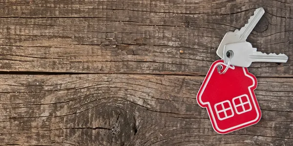 House-shaped keychain with keys resting on weathered wood